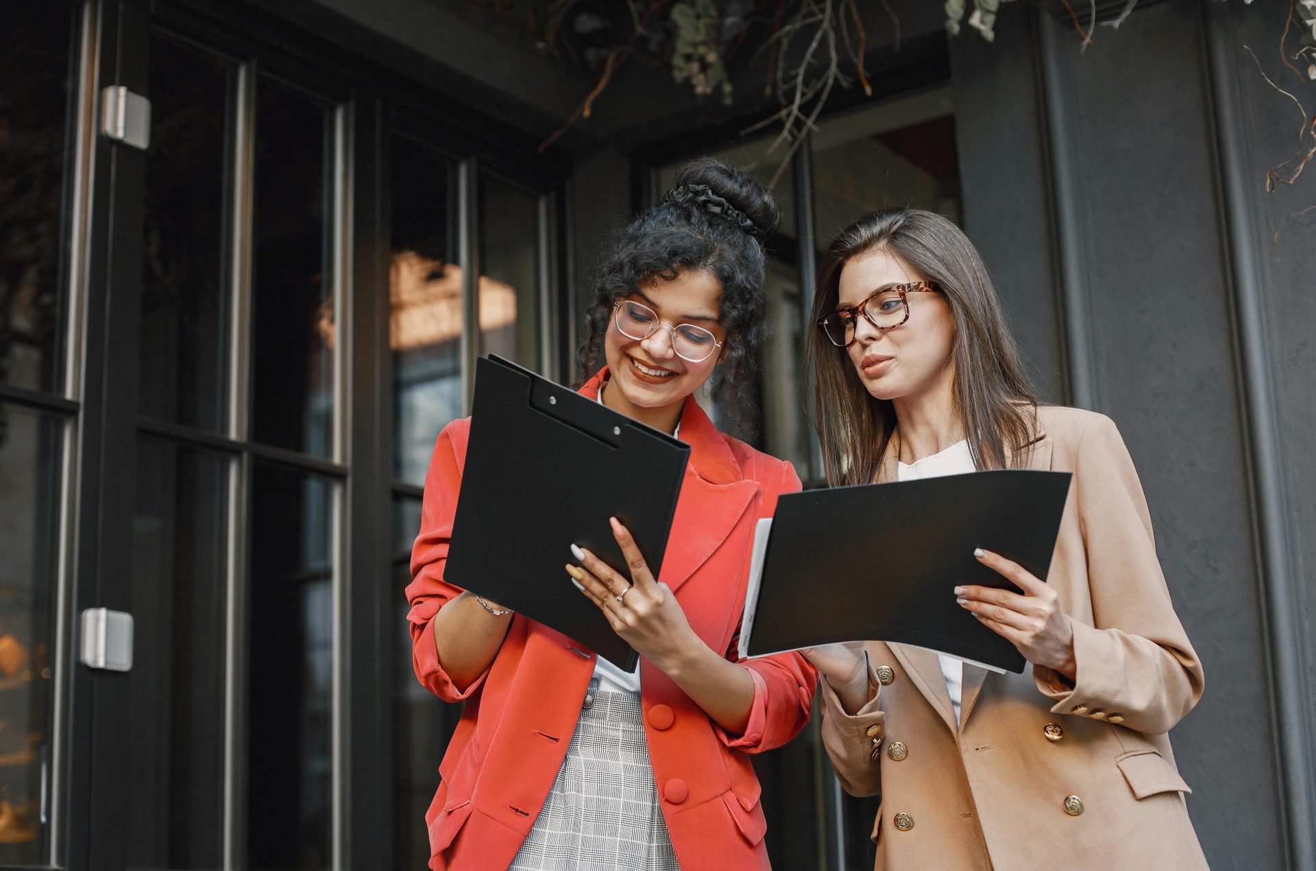 Two businesswomen discussing documents outside in a professional setting.